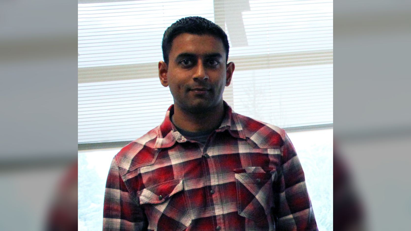 Computer scientist Arvind Narayanan stands indoors wearing a red plaid shirt.