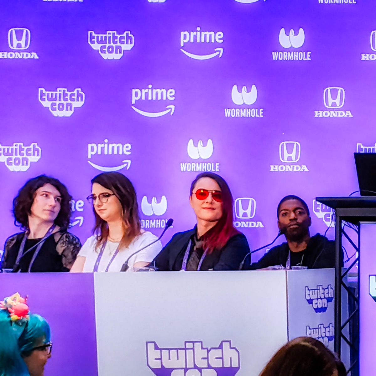 Four creators sit behind a panel desk at TwitchCon 2019, with TwitchCon and Prime logos on the purple backdrop.