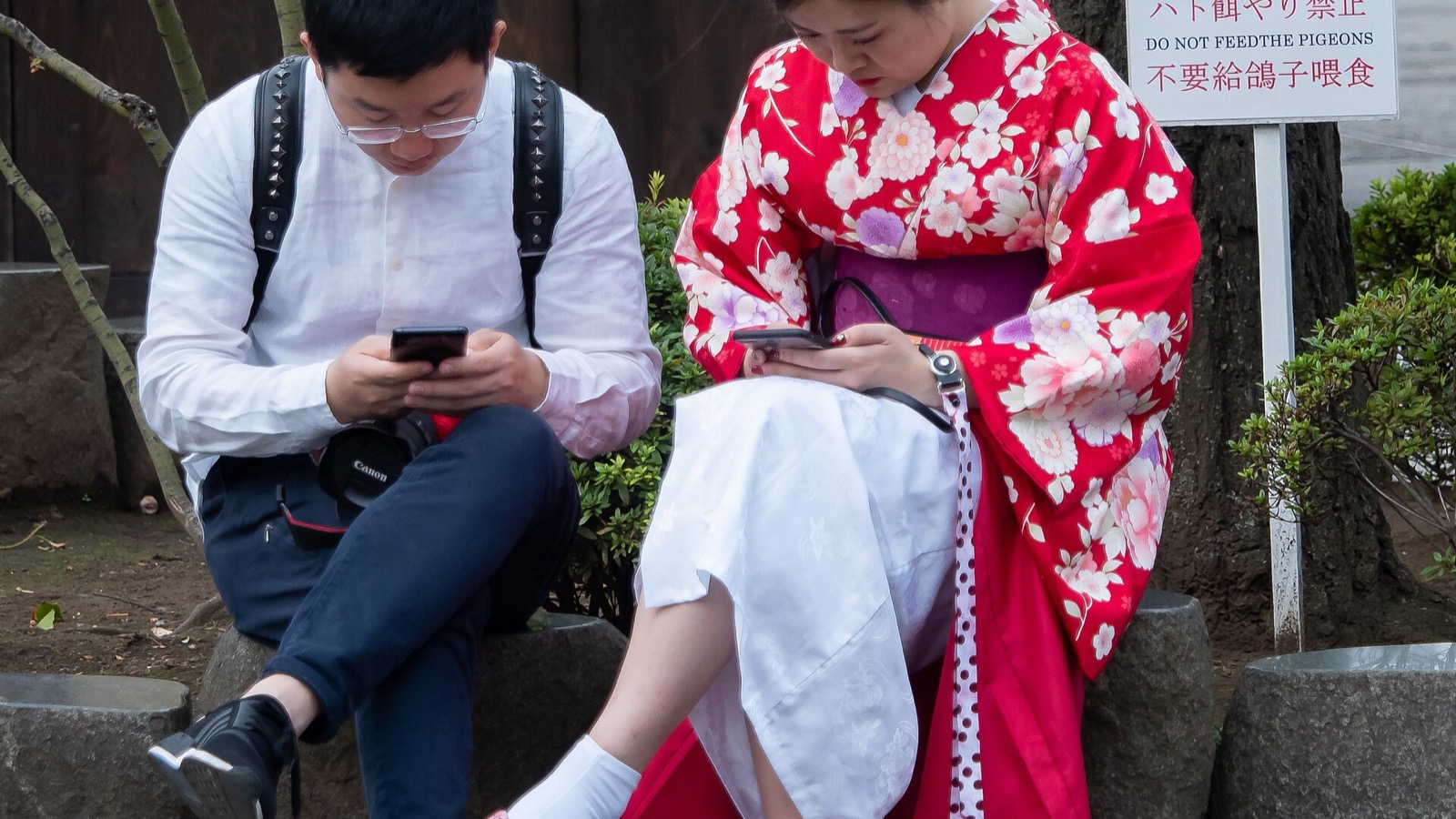 A couple at Senso-ji in Tokyo look at separate mobile phones while standing beside each other.